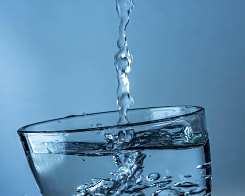 A glass of pure water alongside a notebook on an office table presenting morning hydration balance